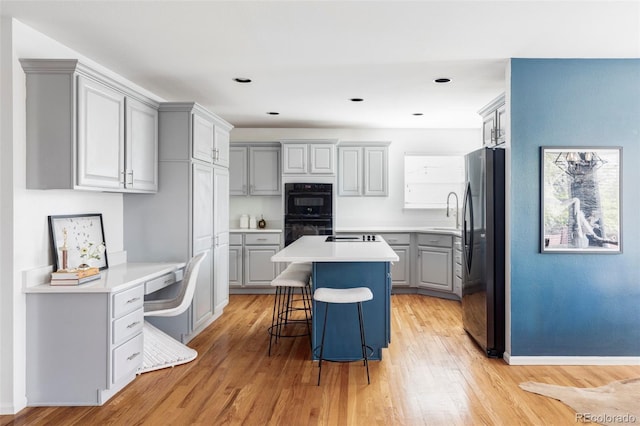 kitchen featuring freestanding refrigerator, gray cabinetry, a center island, a breakfast bar area, and light wood-type flooring