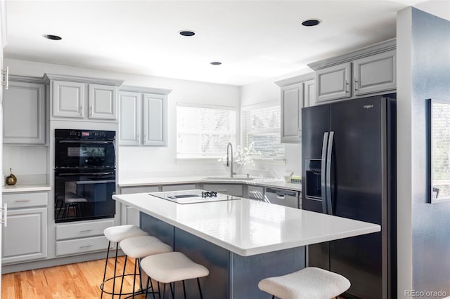 kitchen featuring black appliances, a sink, a kitchen breakfast bar, light countertops, and a center island