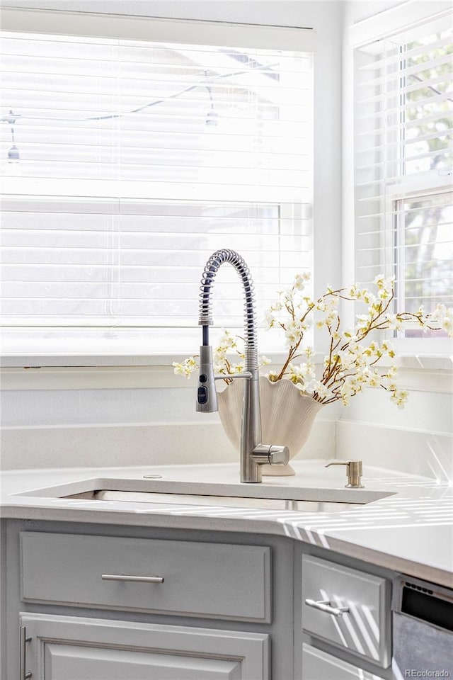 kitchen view of gray cabinetry, a sink, light countertops, and stainless steel dishwasher