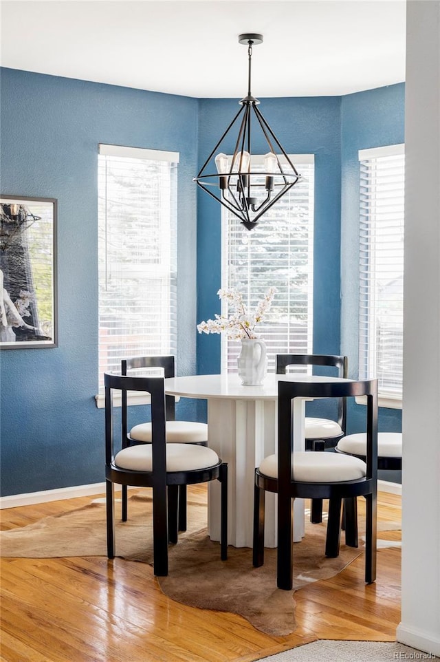 dining space with wood finished floors, a chandelier, a textured wall, and baseboards