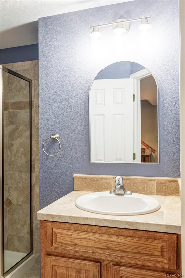 full bathroom with a shower stall, vanity, and a textured wall