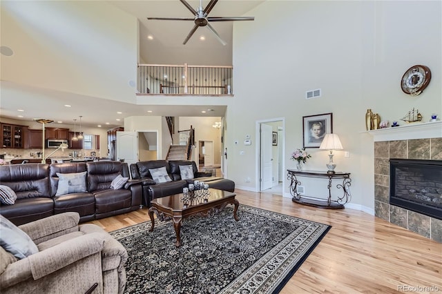 living room with a high ceiling, a fireplace, ceiling fan, and light hardwood / wood-style flooring