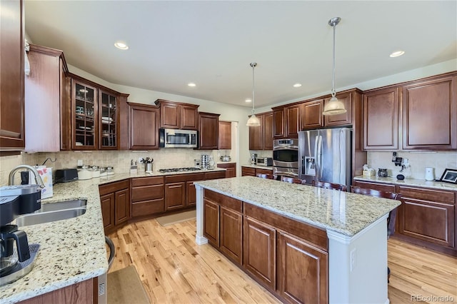 kitchen featuring light stone counters, hanging light fixtures, a kitchen island, appliances with stainless steel finishes, and light wood-type flooring