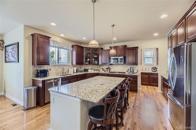 kitchen with appliances with stainless steel finishes, hanging light fixtures, light hardwood / wood-style floors, a center island, and sink