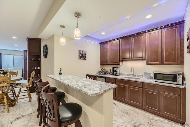 kitchen featuring kitchen peninsula, light stone countertops, pendant lighting, a kitchen bar, and sink