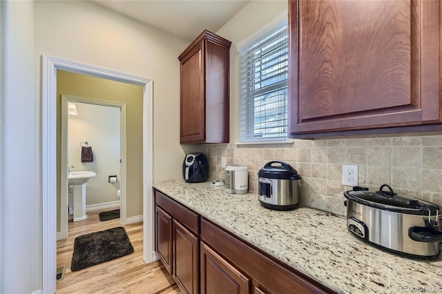 kitchen with light stone counters, light wood-type flooring, and backsplash