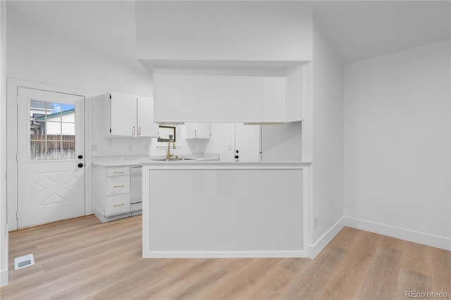 kitchen featuring white dishwasher, a sink, light countertops, light wood-style floors, and white cabinetry