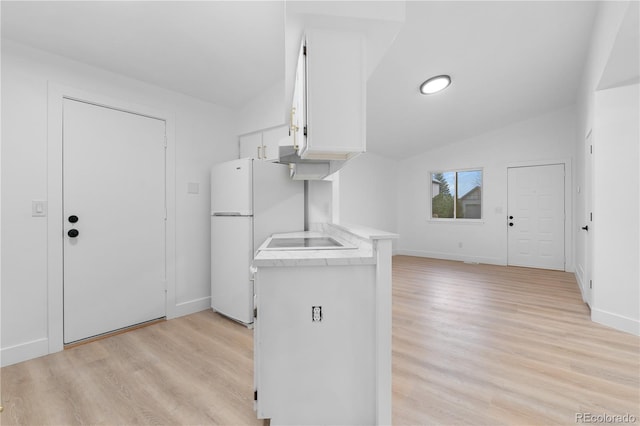 kitchen featuring lofted ceiling, light wood-style flooring, freestanding refrigerator, light countertops, and white cabinets