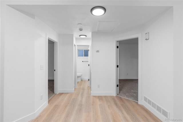 hall with baseboards, visible vents, attic access, and light wood-style floors