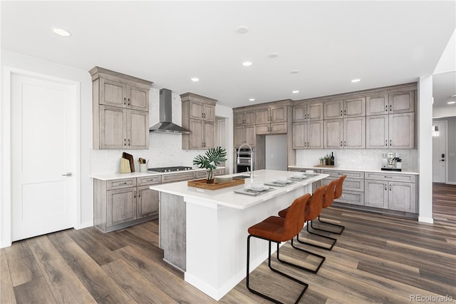 8858 Moonshimmer Trl, Littleton, CO 80125 - kitchen with wall chimney exhaust hood, dark wood-type flooring, recessed lighting, decorative backsplash, and a kitchen island with sink