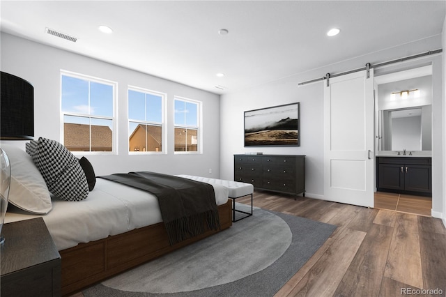 8858 Moonshimmer Trl, Littleton, CO 80125 - bedroom featuring a barn door, wood finished floors, recessed lighting, and connected bathroom