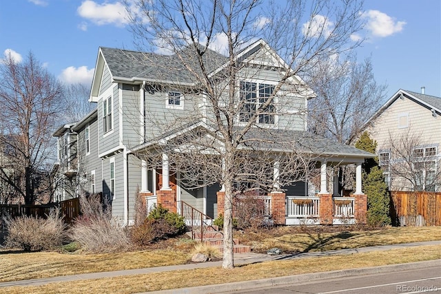 view of front of home with a shingled roof, covered porch, and fence