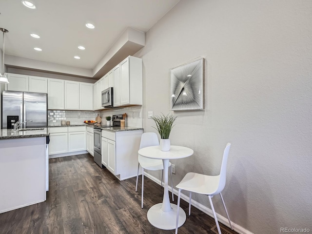 kitchen featuring decorative backsplash, white cabinetry, stainless steel appliances, and dark stone counters