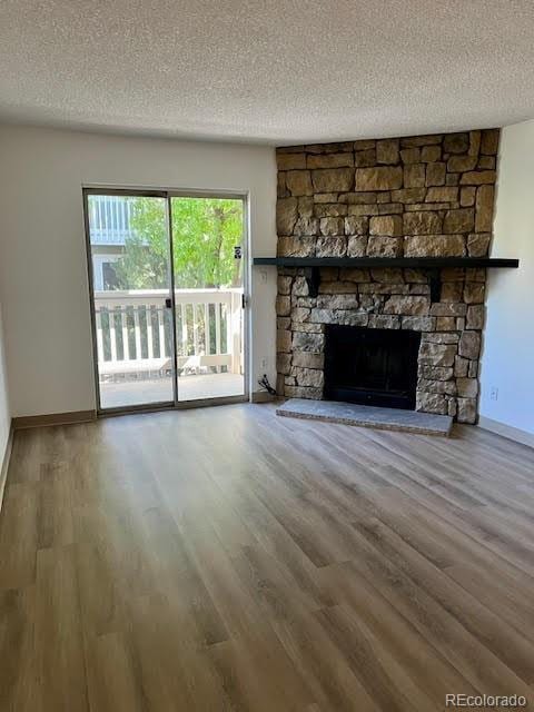4400 S Quebec St Unit 102R, Denver, CO 80237 - unfurnished living room featuring a textured ceiling, baseboards, wood finished floors, and a stone fireplace