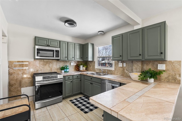 kitchen with light tile patterned flooring, sink, tile counters, stainless steel appliances, and beam ceiling