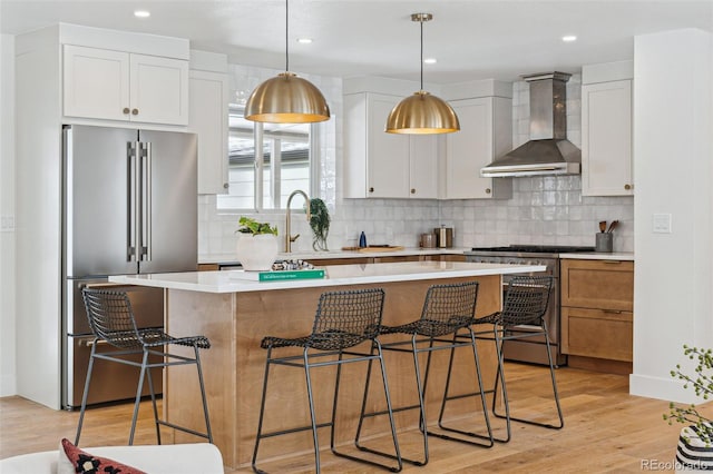 kitchen featuring high end appliances, wall chimney exhaust hood, white cabinets, and a center island