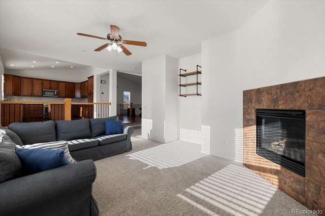 carpeted living room with a tiled fireplace, ceiling fan, and vaulted ceiling