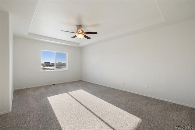 spare room with a raised ceiling, ceiling fan, and carpet