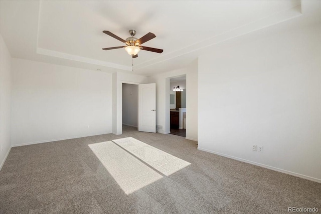 unfurnished bedroom featuring a tray ceiling, ensuite bathroom, carpet flooring, and ceiling fan with notable chandelier