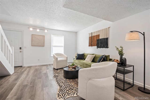 living area featuring stairway, baseboards, a textured ceiling, and wood finished floors