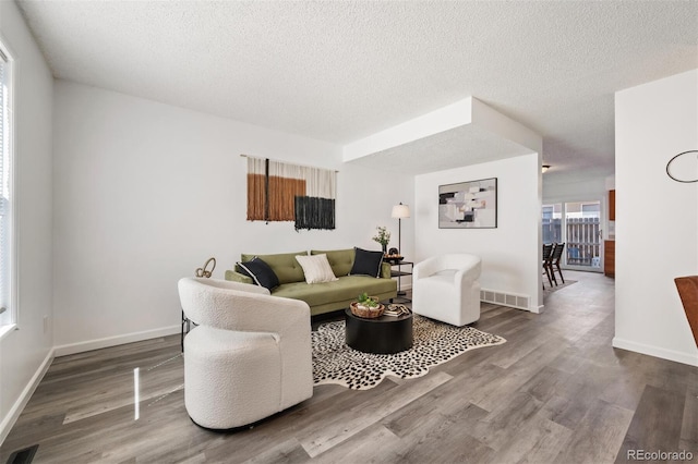 living area with visible vents, a textured ceiling, and wood finished floors