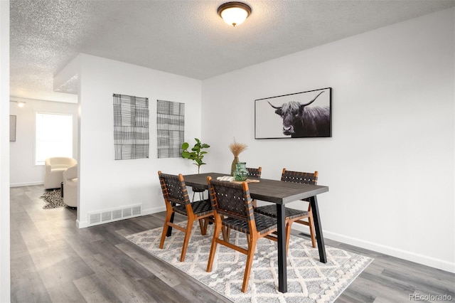 dining area with baseboards, wood finished floors, visible vents, and a textured ceiling