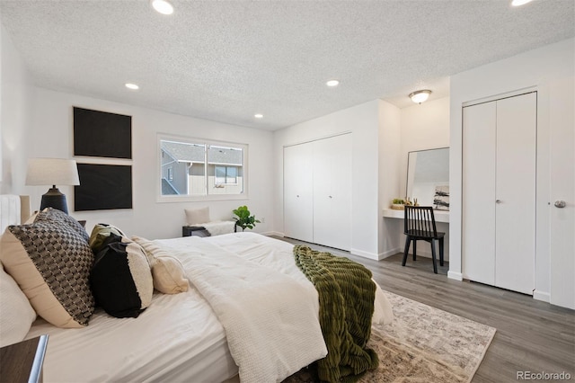 bedroom with wood finished floors, baseboards, recessed lighting, a textured ceiling, and two closets