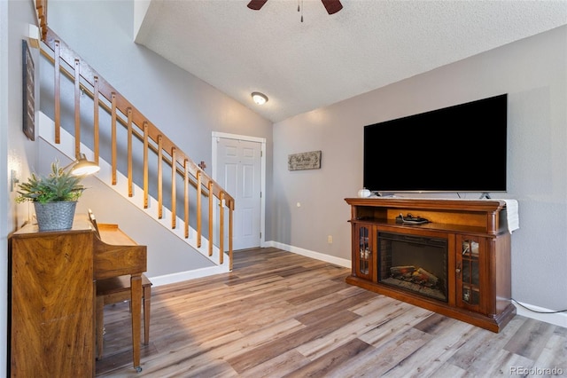 living area with stairway, a textured ceiling, lofted ceiling, and wood finished floors