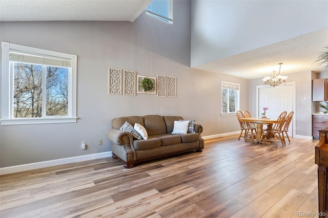 living area featuring light wood-style flooring, a notable chandelier, baseboards, and a textured ceiling