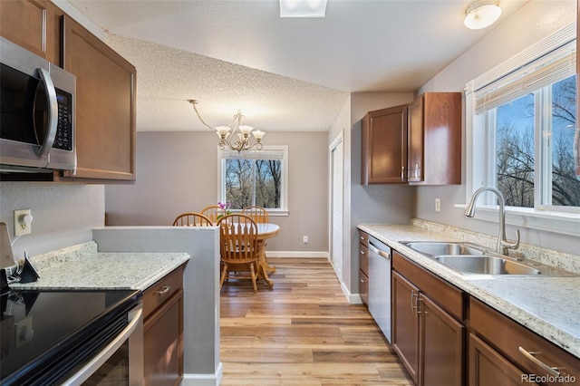 kitchen with baseboards, light wood-style flooring, a sink, stainless steel appliances, and a textured ceiling