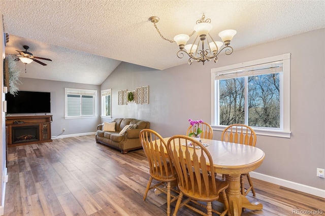 dining space featuring vaulted ceiling, a fireplace, baseboards, and wood finished floors