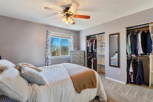 carpeted bedroom with baseboards, a ceiling fan, multiple closets, and a textured ceiling