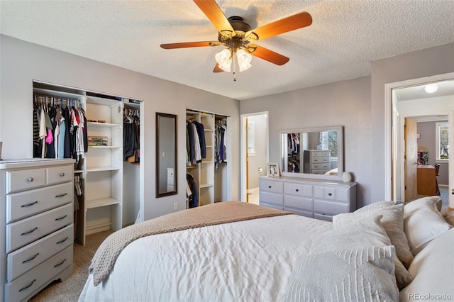 carpeted bedroom with a ceiling fan, multiple closets, and a textured ceiling