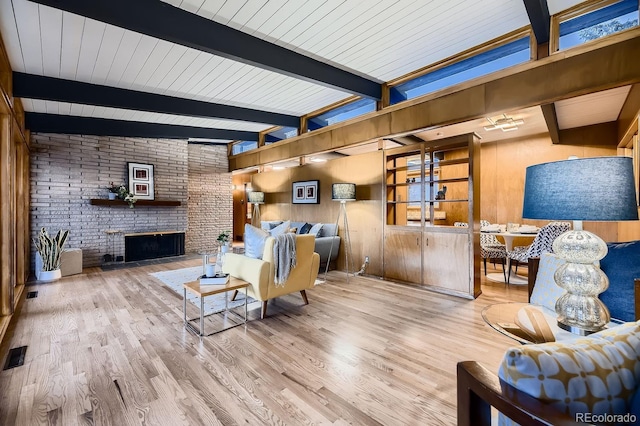 living room featuring beamed ceiling, wood-type flooring, a brick fireplace, and wood walls