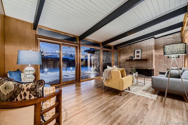 living room with wood ceiling, lofted ceiling with beams, a brick fireplace, light wood-type flooring, and wooden walls