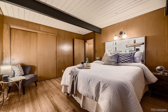 bedroom featuring beamed ceiling, light hardwood / wood-style flooring, and wood walls