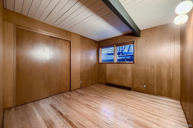 interior space featuring beam ceiling, light hardwood / wood-style flooring, a closet, and wood walls