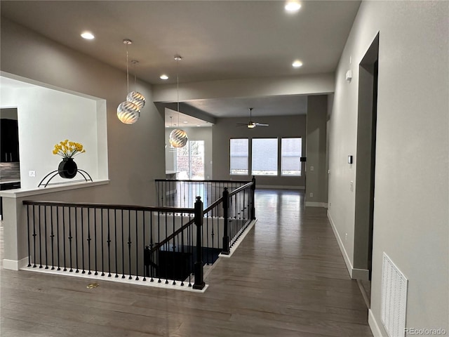 hallway featuring wood finished floors, visible vents, baseboards, recessed lighting, and an upstairs landing