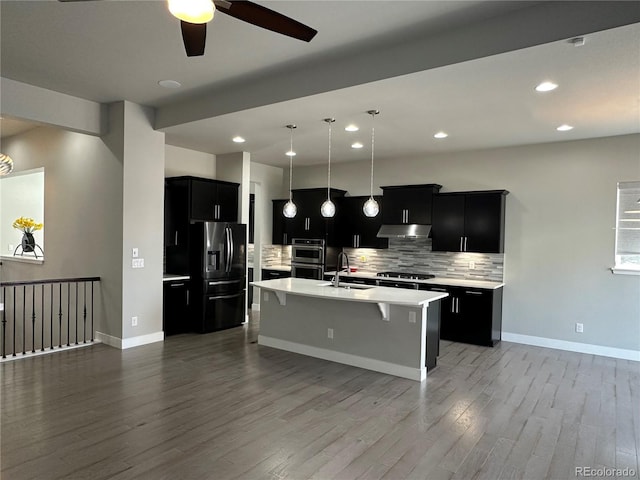 kitchen with a breakfast bar, a sink, under cabinet range hood, dark cabinets, and black refrigerator with ice dispenser