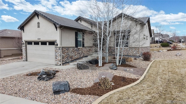 view of front of property with stucco siding, concrete driveway, an attached garage, stone siding, and a tiled roof