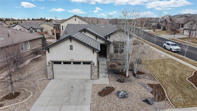 view of front of home with an attached garage, stone siding, concrete driveway, a residential view, and stucco siding