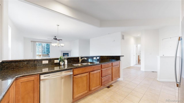 kitchen featuring brown cabinets, visible vents, stainless steel dishwasher, a sink, and dark stone counters