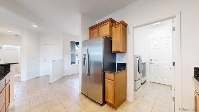 kitchen with light tile patterned floors, baseboards, stainless steel fridge with ice dispenser, brown cabinetry, and washer / dryer