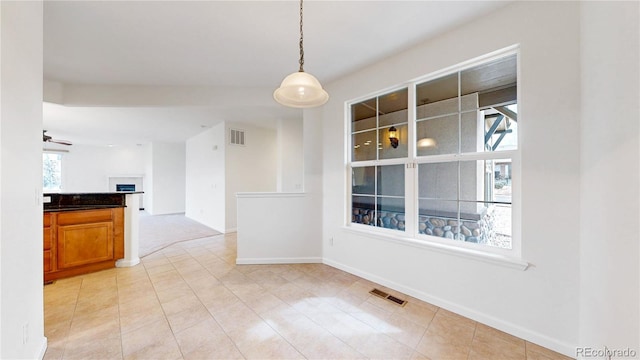 unfurnished dining area featuring a ceiling fan, visible vents, a fireplace, and baseboards