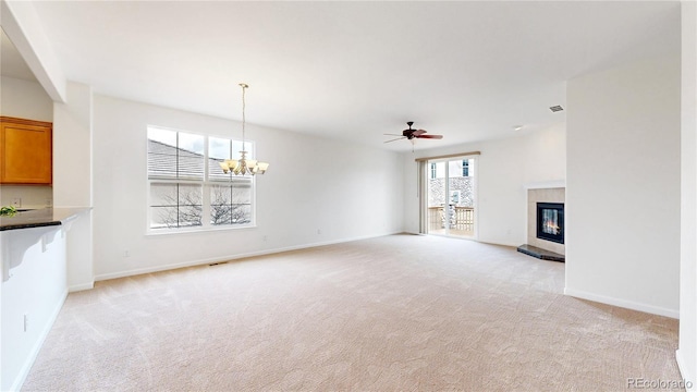 unfurnished living room featuring light carpet, ceiling fan with notable chandelier, a tiled fireplace, and baseboards