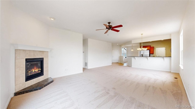 unfurnished living room with light colored carpet, ceiling fan with notable chandelier, visible vents, baseboards, and a tiled fireplace