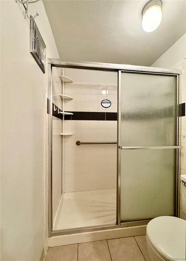 bathroom featuring tile patterned flooring, toilet, and a shower with door