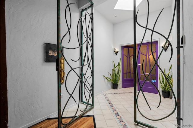 tiled foyer featuring a skylight, a textured wall, and baseboards