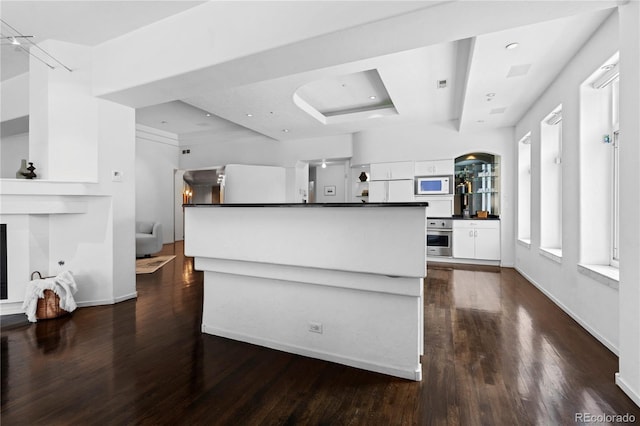 kitchen with white microwave, white cabinetry, dark countertops, a tray ceiling, and stainless steel oven