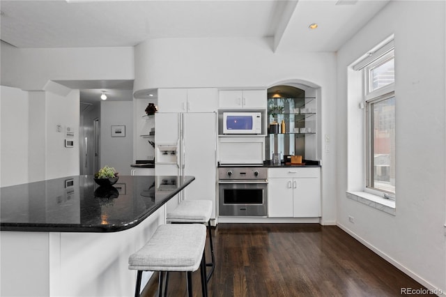 kitchen featuring white cabinets, white appliances, a breakfast bar, and dark wood finished floors